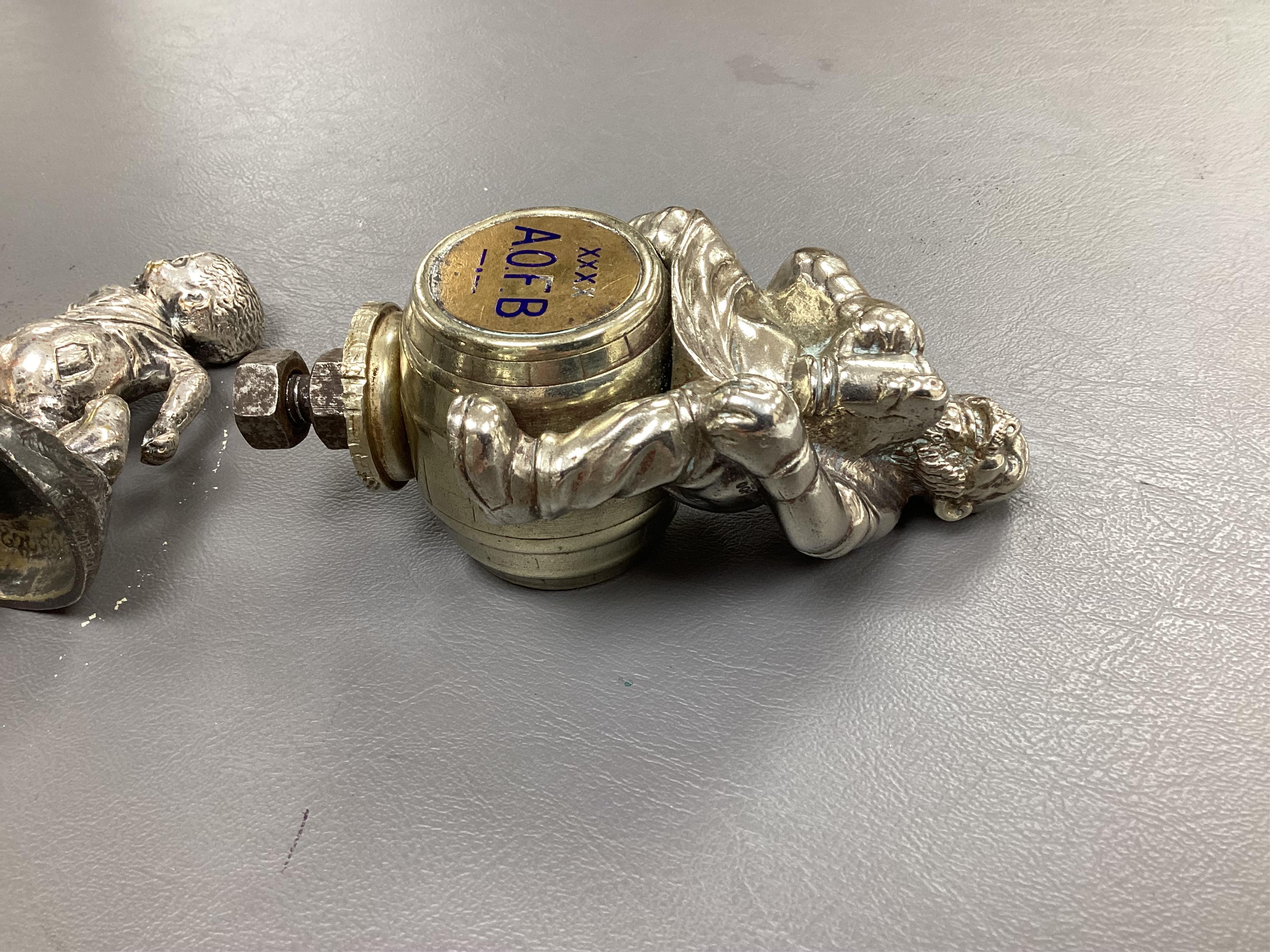 Seven chrome and brass car mascots, including a Mercedes-Benz logo, a figure of a blacksmith, a caricature figure on a beer barrel, a golf ball in mid flight, etc. together with a chromed housing unit for an electric lam